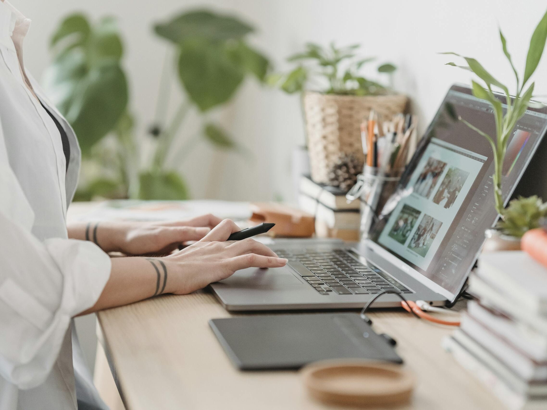 Freelance designer working from home using a laptop and digital tablet, surrounded by plants.